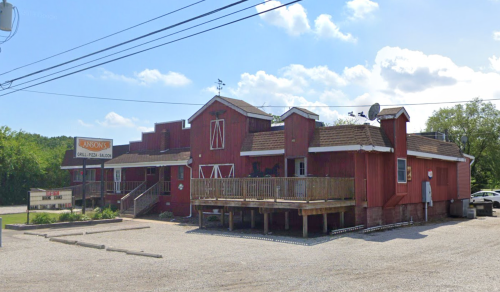 A red building with a wooden deck, surrounded by gravel and trees, under a blue sky with scattered clouds.