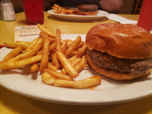 A plate with a burger and a side of golden French fries on a yellow table.