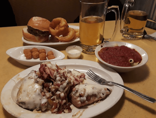A table with a burger, onion rings, beer, tater tots, and a plate of cheesy meat with marinara sauce.