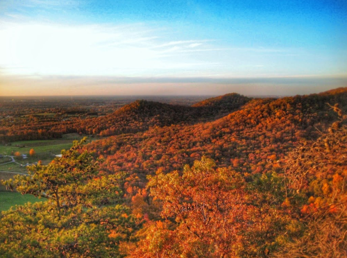 A scenic view of rolling hills covered in autumn foliage under a clear blue sky at sunset.