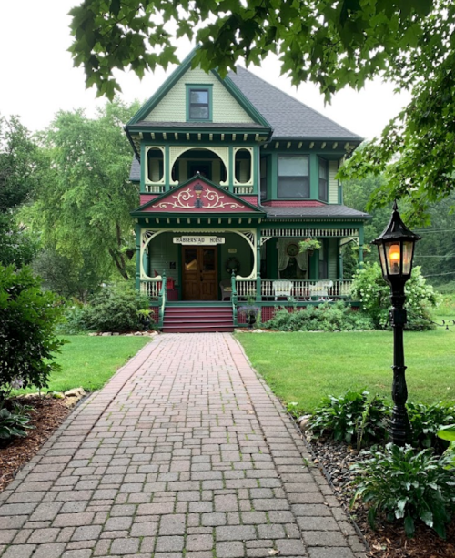A charming Victorian-style house with intricate details, surrounded by greenery and a pathway leading to the entrance.