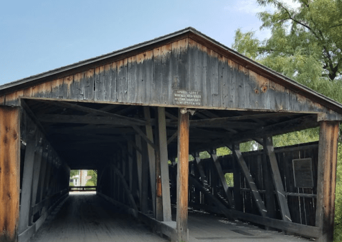 A weathered wooden covered bridge with a clear blue sky in the background.