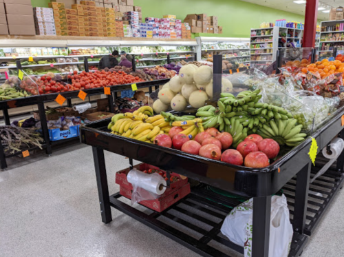 A grocery store display featuring various fruits, including bananas, pomegranates, melons, and tomatoes on shelves.