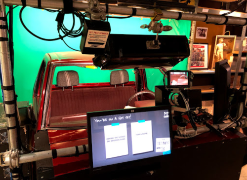 A car set with a green screen backdrop, cameras, and monitors for filming or production purposes.
