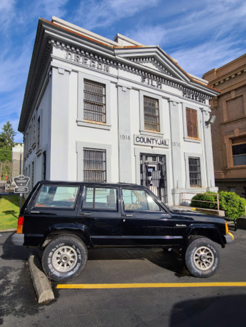 A black SUV parked in front of a historic county jail building with barred windows and a sign.