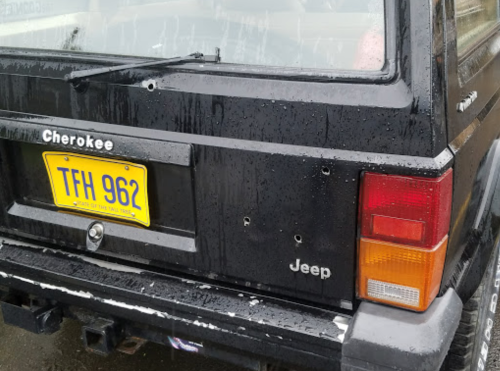 A black Jeep Cherokee with a wet surface and a visible license plate, showing signs of wear and damage.