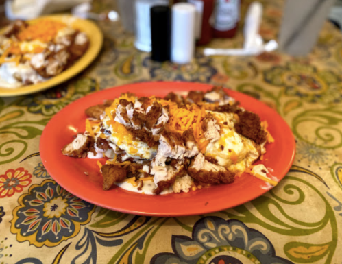 A colorful plate of scrambled eggs topped with shredded cheese and pieces of fried chicken, served on a patterned tablecloth.