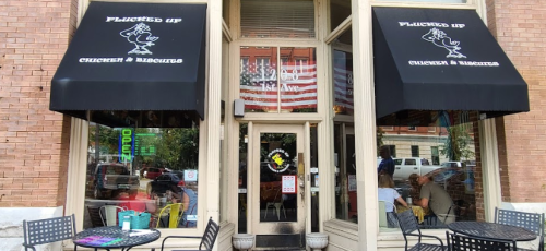 Exterior of "Plucked Up Chicken & Biscuits" with black awnings, showcasing outdoor seating and a view of the street.