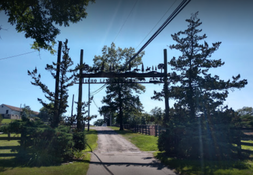 A wooden entrance sign surrounded by trees, leading to a pathway on a sunny day.
