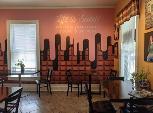 A cozy café interior with a chocolate-themed wall mural and wooden tables, creating a warm, inviting atmosphere.