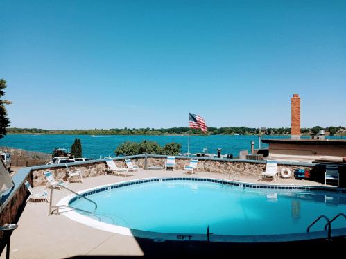 A clear blue pool with lounge chairs, overlooking a lake and a flag waving in the breeze under a bright blue sky.