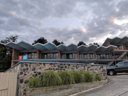 A modern building with a zigzag roof design, featuring large windows and a stone wall in the foreground.