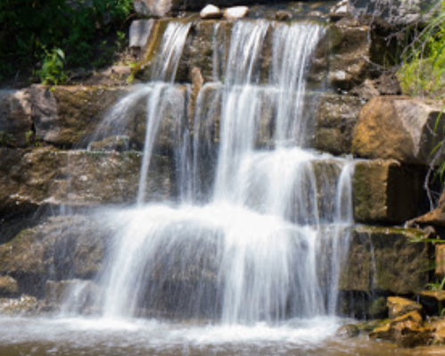 A serene waterfall cascading over rocky steps, surrounded by lush greenery.