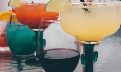 A variety of colorful cocktails in glasses, including margaritas and a dark drink, on a table.