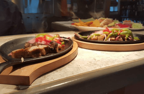 Two sizzling fajita platters with grilled meat, bell peppers, and onions on wooden serving boards.