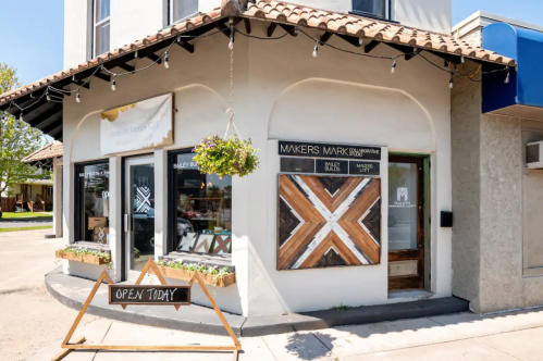 A storefront with a sign reading "Makers Mark" and an "Open Today" sign outside, featuring a decorative wooden design.