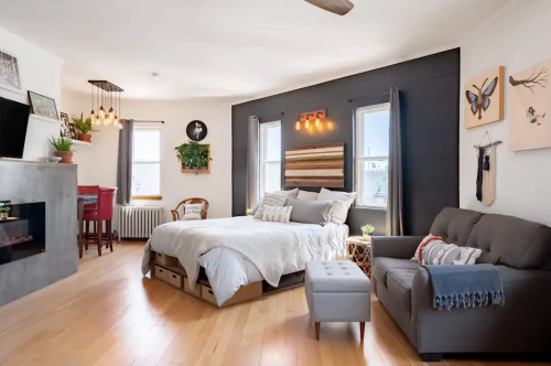 Cozy bedroom featuring a bed, sofa, and decorative wall art, with natural light and wooden flooring.