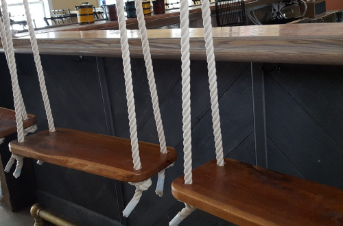 A wooden swing seat hangs from a rope, attached to a bar counter in a modern setting.