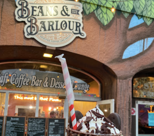 A delicious dessert drink topped with whipped cream and a straw, in front of a colorful café sign.