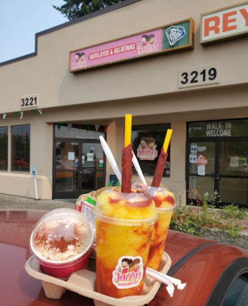 Four colorful desserts in a tray outside a shop, with a sign reading "Jazzy's Antojitos & Gelatinas" in the background.