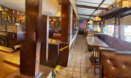 Interior of a rustic restaurant featuring wooden beams, tables, and an American flag in the background.