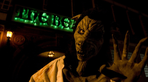A menacing creature with wolf-like features stands outside a dimly lit pub, "The Bell," with green neon lights.