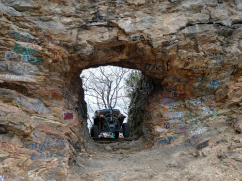 A rugged rock formation with graffiti, framing an off-road vehicle in the distance.