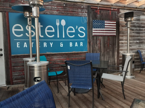 Outdoor seating area at Estelle's Eatery & Bar, featuring a blue sign and an American flag on the wall.