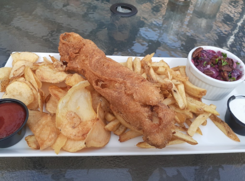 A plate of crispy fried fish with potato chips, French fries, and a side of coleslaw and dipping sauces.