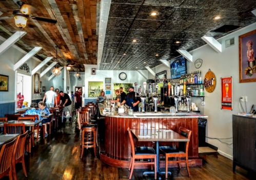 A cozy restaurant interior with a bar, wooden tables, and patrons enjoying their meals in a warm atmosphere.