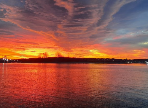 Vibrant sunset over a calm lake, with orange, pink, and purple hues reflecting on the water's surface.