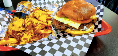 A tray with a crispy chicken sandwich and cheesy fries, both served in checkered paper.