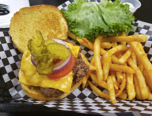 A cheeseburger with lettuce, tomato, pickles, and onion on a toasted bun, served with crispy French fries.