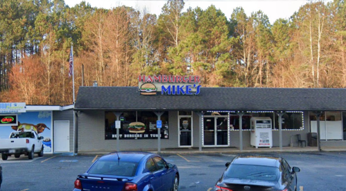 A restaurant named "Hamburger Mike's" with a sign featuring a burger, surrounded by trees and parked cars.