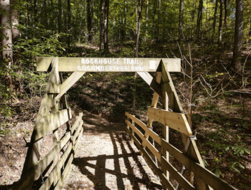 Wooden sign for Rockhouse Trail at the entrance of a forest path, surrounded by trees and greenery.