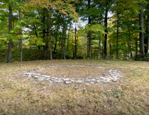 A circular stone arrangement on grassy ground, surrounded by trees with autumn foliage.