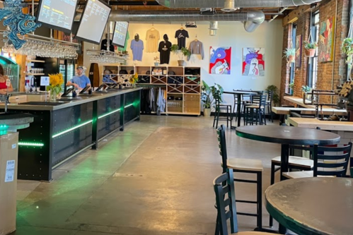 A spacious bar area with tables, a counter, and colorful artwork on the walls, featuring a staff member in the background.