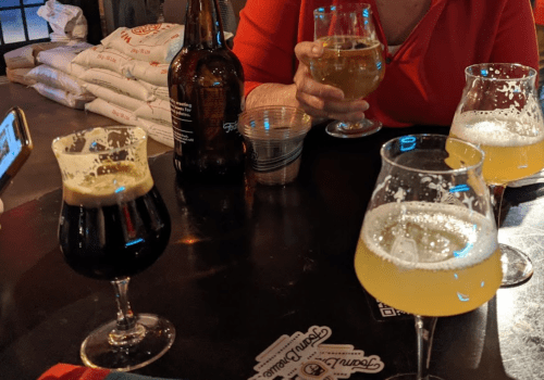 A table with various glasses of beer, including dark and light brews, and a bottle in the background.