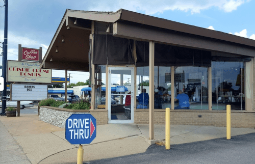 A coffee shop with a drive-thru, featuring large windows and a sign displaying "Drive Thru" and "Bakers Dozen."