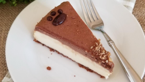 A slice of chocolate cheesecake with a graham cracker crust, topped with a chocolate paw print, on a white plate.