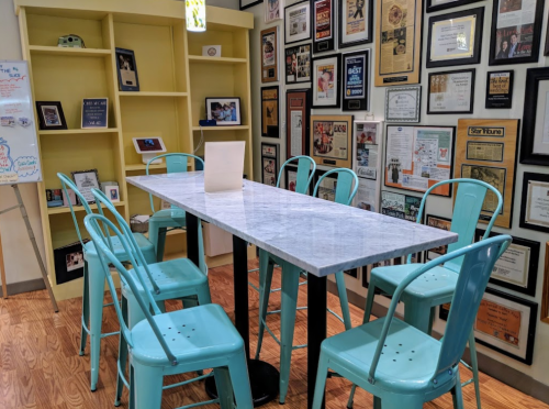 A modern dining area with a marble table and turquoise chairs, surrounded by framed certificates on the walls.