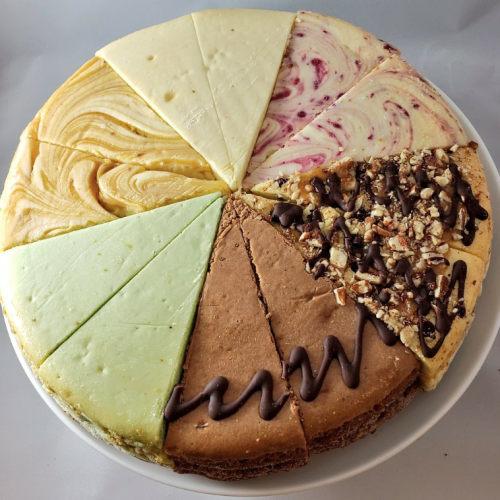 A round cheesecake with eight different slices, featuring various flavors and toppings, arranged on a white plate.
