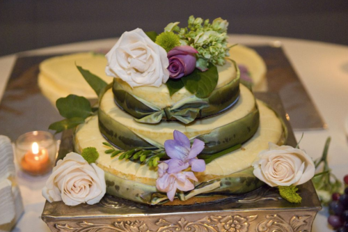 A three-tiered cake decorated with flowers and greenery, displayed on an elegant silver stand.