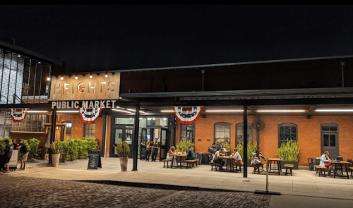 A lively public market at night, featuring outdoor seating and festive decorations.