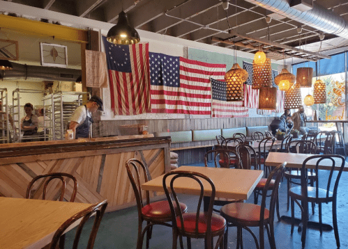 Interior of a restaurant featuring wooden tables, chairs, and multiple American flags hanging on the walls.