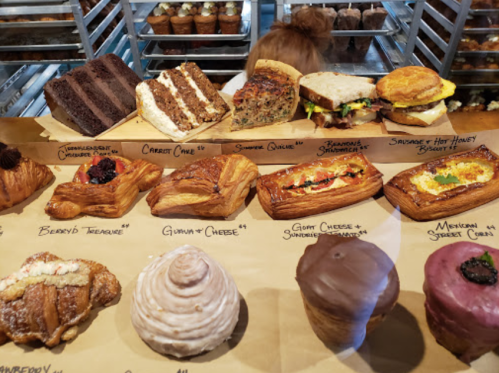 A display of various baked goods, including cakes, pastries, and savory items, arranged on a parchment-lined counter.