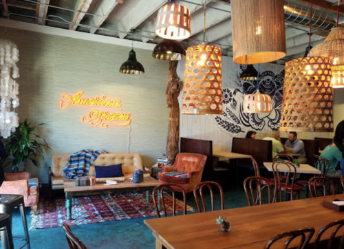 Cozy restaurant interior with warm lighting, wooden furniture, and a neon sign reading "American Gypsy."