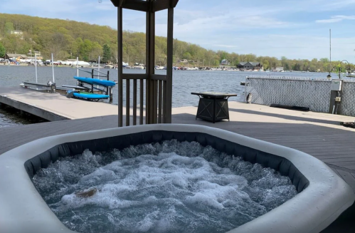 A hot tub on a deck overlooking a calm lake with boats and green hills in the background.
