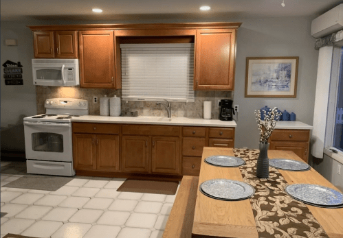 A cozy kitchen with wooden cabinets, a white stove, and a dining table set with blue plates and a floral centerpiece.