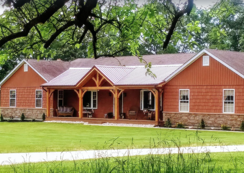 A charming red house with a porch, surrounded by greenery and a well-maintained lawn.